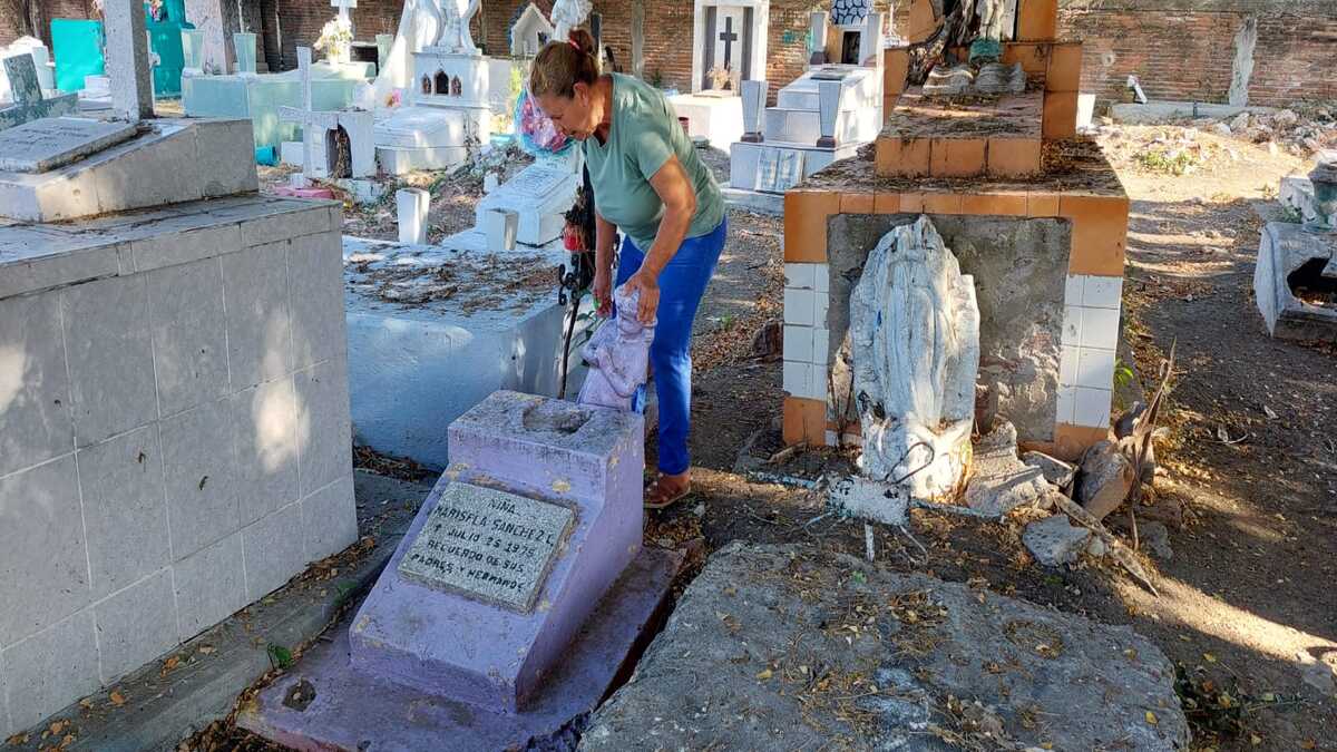 La señora Guadalupe reparte las flores que le lleva a su hija al panteón con una tumba abandonada de una niña